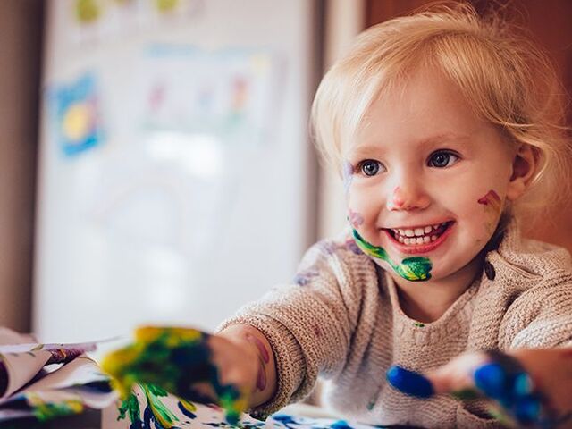 Un bimbo piccolo tutto imbrattato di colori sul viso e sulle dita