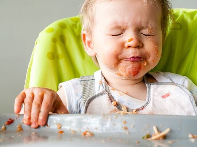 Un bambino piccolo a tavola con il viso tutto sporco.