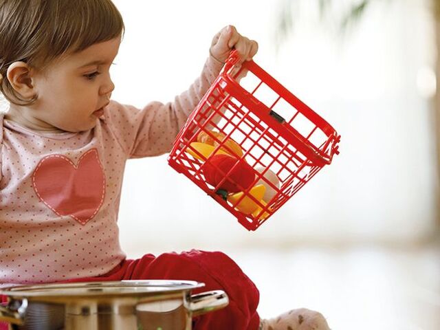 Una bimba piccola gioca con una pentola e degli ortaggi giocattolo.