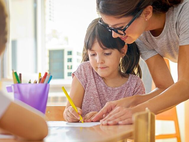 Una maestra di scuola dell’infanzia aiuta due bimbi.