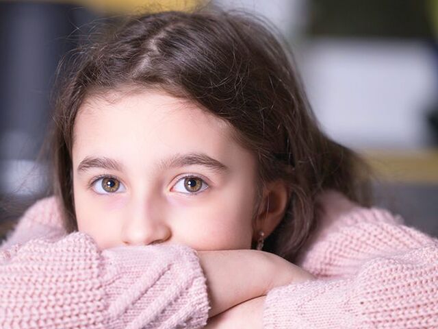 Una bimba con la testa appoggiata sulle braccia guarda pensierosa verso l’obiettivo.