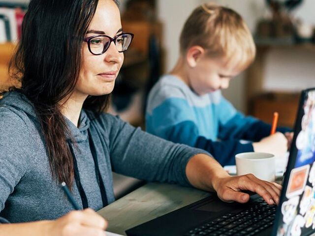 Una mamma intenta a lavorare da casa con il figlio seduto accanto.