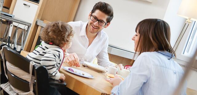 Une mère et un père sont assis à table avec leur enfant et mangent.