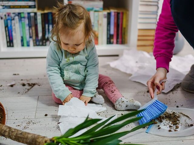 Una bimba seduta vicino a un vaso di fiori rovesciato.