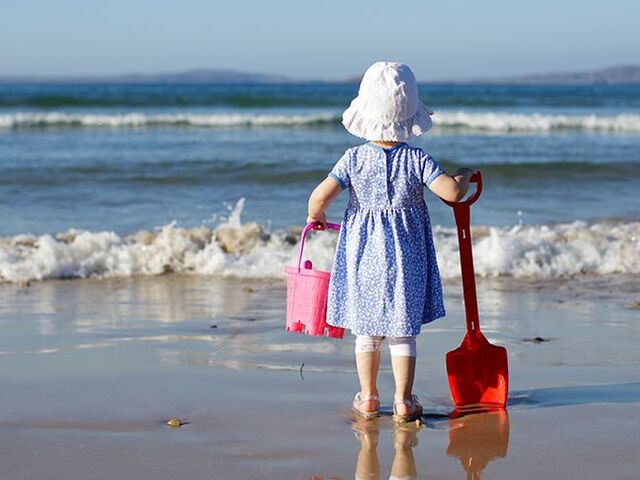Una bimba in piedi sulla spiaggia che guarda il mare.