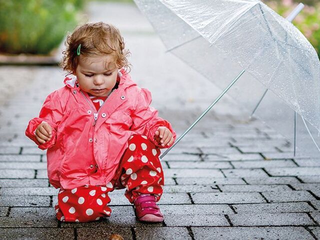 Una bimba piccola con un ombrello che osserva una lumaca.