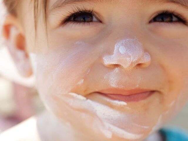 Un bimbo piccolo con un cappellino e la crema solare sul viso.