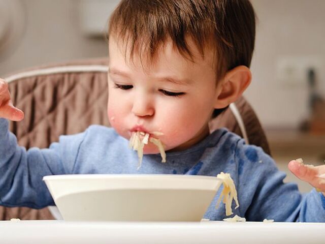 Un bimbo piccolo mangia un piatto di pasta con le mani.