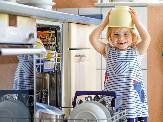 Una bimba con una scodella in testa svuota la lavastoviglie.