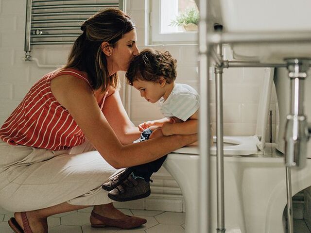 Una mamma sorregge il suo piccolo seduto sul WC.
