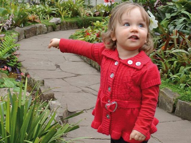 Una bimba piccola in piedi su un vialetto indica delle piante.
