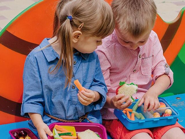 Une petite fille et un petit garçon mangent leurs dix-heures à l’école.