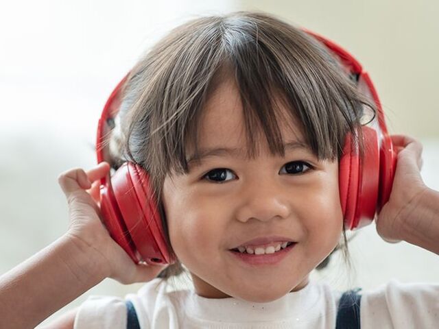 Una bimba si preme sulle orecchie delle cuffie rosse e sorride.