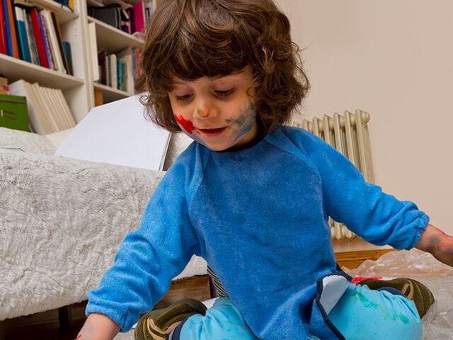 Una bimba dipinge con le dita su un grande foglio di carta steso su un pavimento protetto da una copertura.