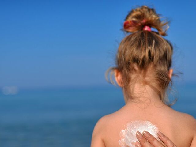 Un bimbo si fa spalmare la crema solare sulla schiena.