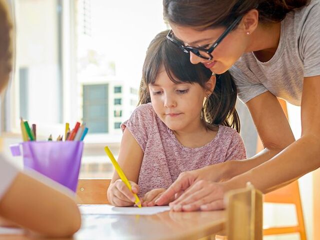 Una maestra di scuola dell’infanzia aiuta due bimbi.