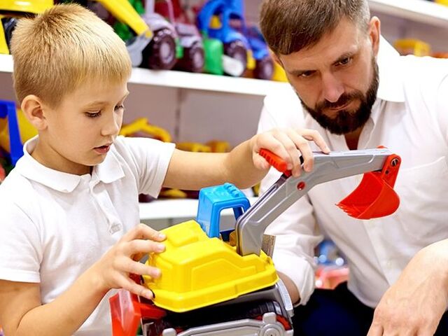 Un bimbo e il papà osservano attentamente un escavatore in un negozio di giocattoli.
