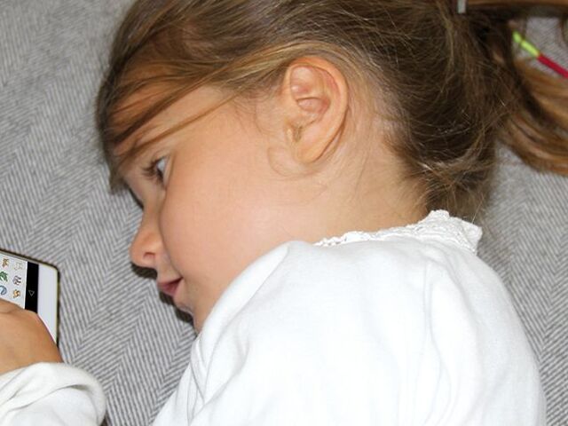 Una bimba sul divano invia emoji da un cellulare.