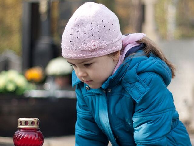 Una bambina osserva attentamente una tomba in un cimitero.