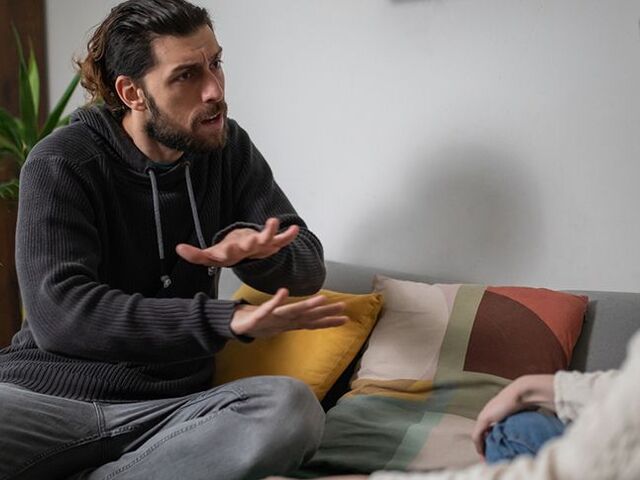 Una mamma e un papà sul divano gesticolano animatamente mentre discutono.
