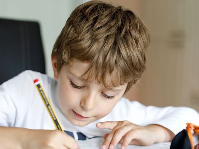 Un bimbo scrive con la matita su un quaderno.